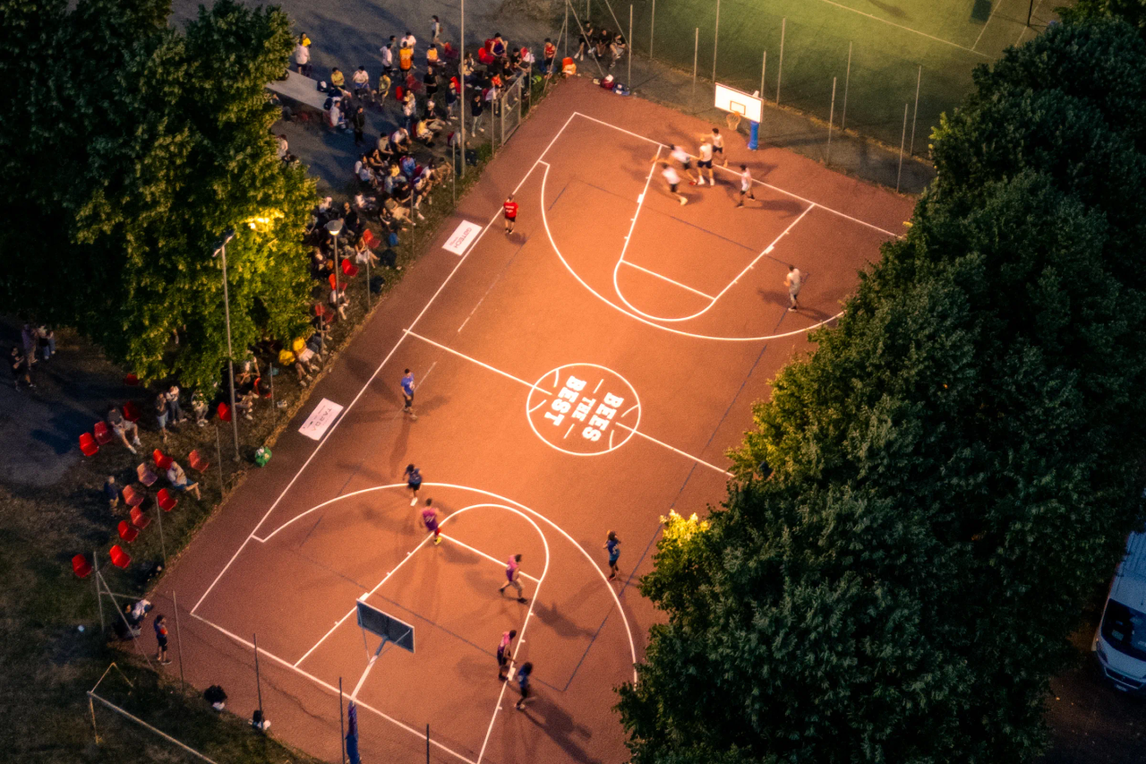 Il campo di Bees The Best visto dall'alto di sera: partita in corso, la scritta Bees The Best al centro e il pubblico a bordo campo